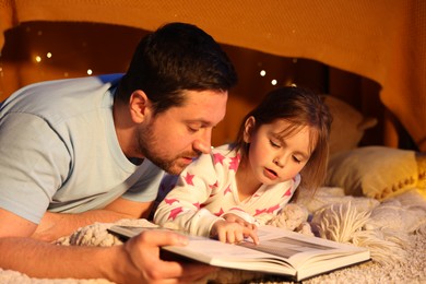 Photo of Father reading bedtime story to his daughter on floor at home