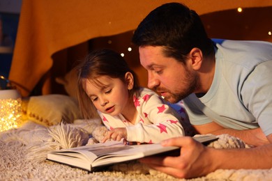 Photo of Father reading bedtime story to his daughter on floor at home