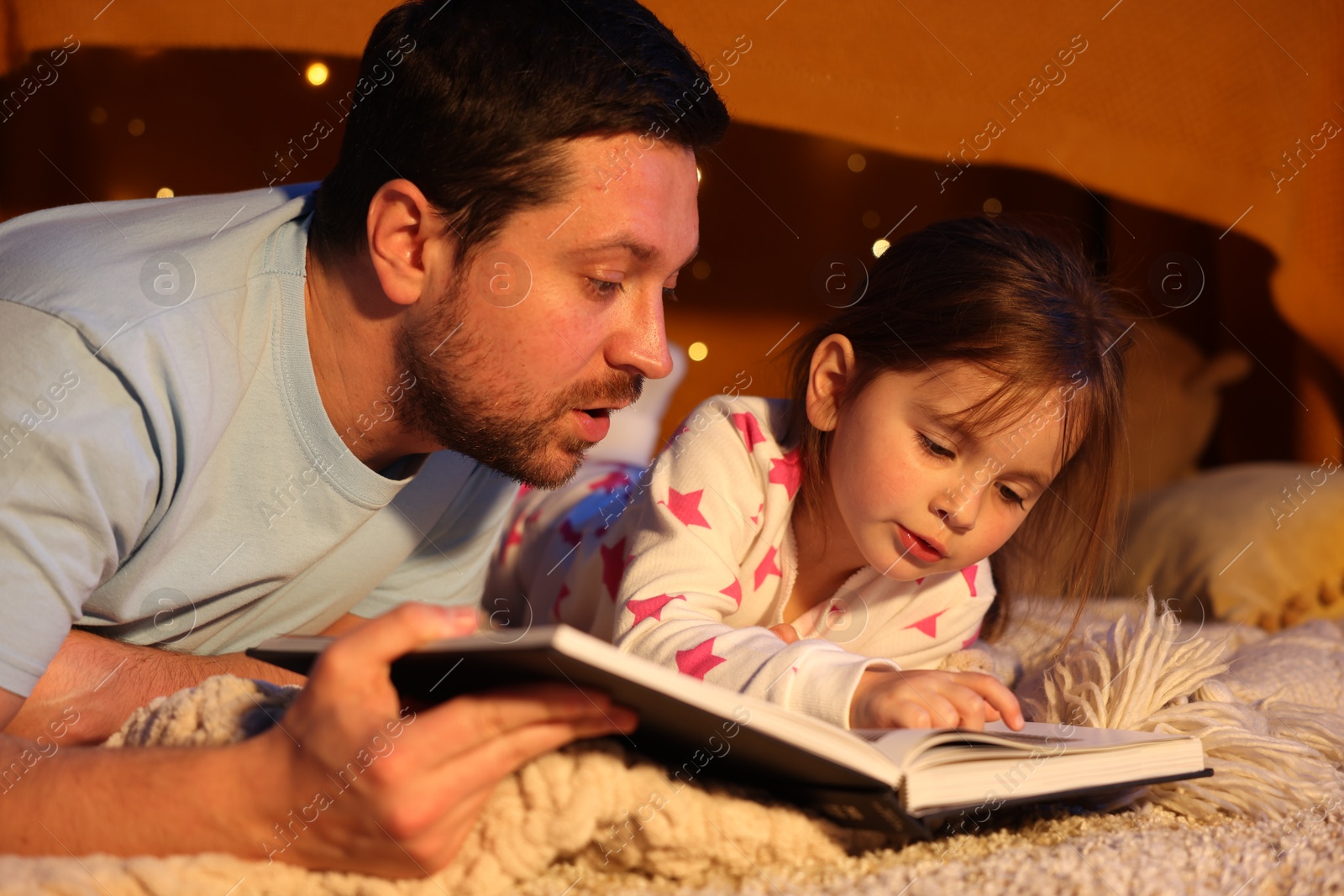 Father reading bedtime story to his daughter on floor at home Photo of Father reading bedtime story to his daughter on floor at home