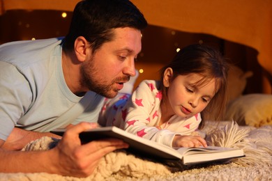 Photo of Father reading bedtime story to his daughter on floor at home