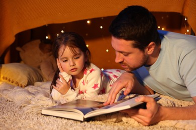 Photo of Father reading bedtime story to his daughter on floor at home