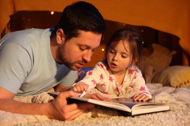 Photo of Father reading bedtime story to his daughter on floor at home