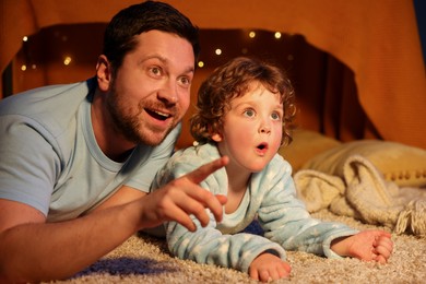Photo of Happy father and his son pointing at something at home. Bedtime