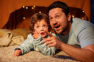 Photo of Happy father and his son pointing at something at home. Bedtime