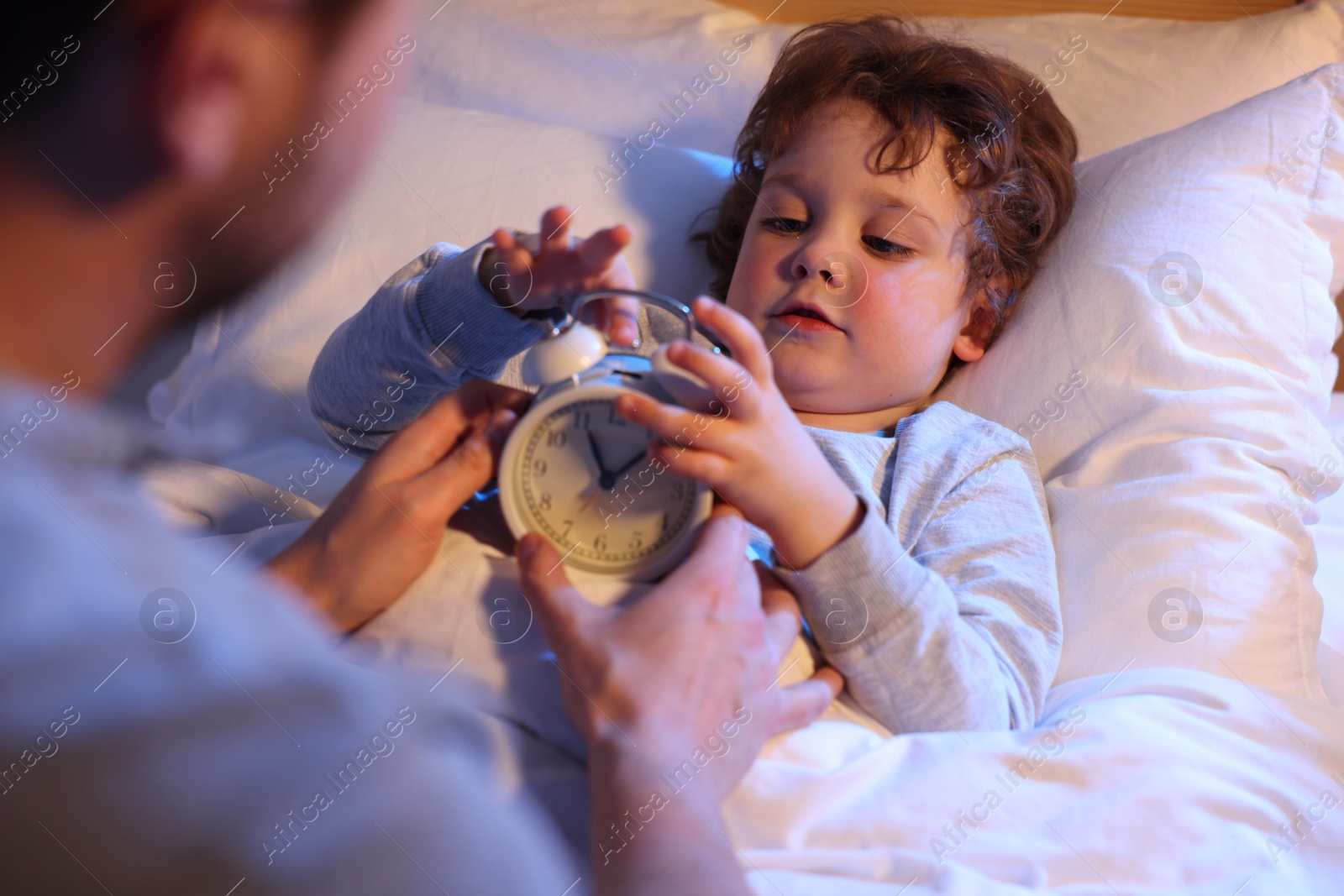 Father and his little son with alarm clock on bed, selective focus. Bedtime Photo of Father and his little son with alarm clock on bed, selective focus. Bedtime