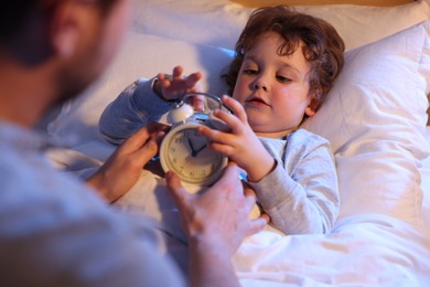 Photo of Father and his little son with alarm clock on bed, selective focus. Bedtime