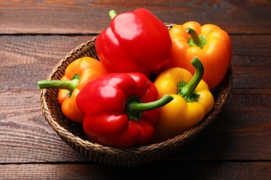 Photo of Fresh colorful bell peppers in wicker basket on wooden table, closeup