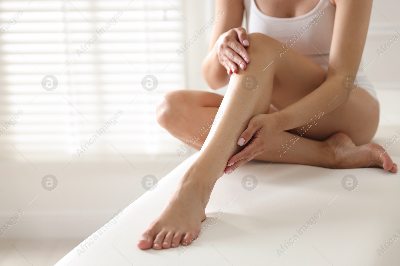 Woman with beautiful smooth legs after epilation on bed indoors, closeup. Space for text Photo of Woman with beautiful smooth legs after epilation on bed indoors, closeup. Space for text