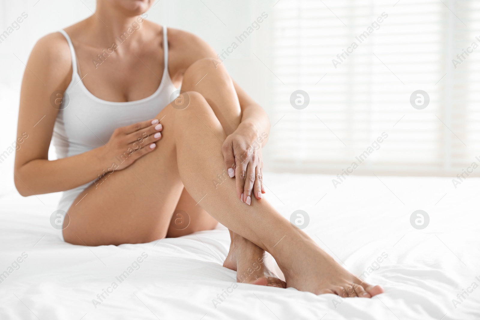 Woman with beautiful smooth legs after epilation on bed at home, closeup. Space for text Photo of Woman with beautiful smooth legs after epilation on bed at home, closeup. Space for text