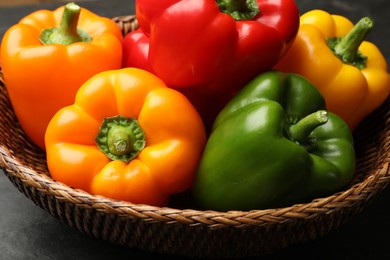 Photo of Fresh colorful bell peppers in wicker basket on dark table, closeup