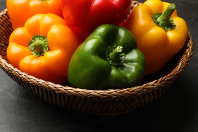 Photo of Fresh colorful bell peppers in wicker basket on dark table, closeup