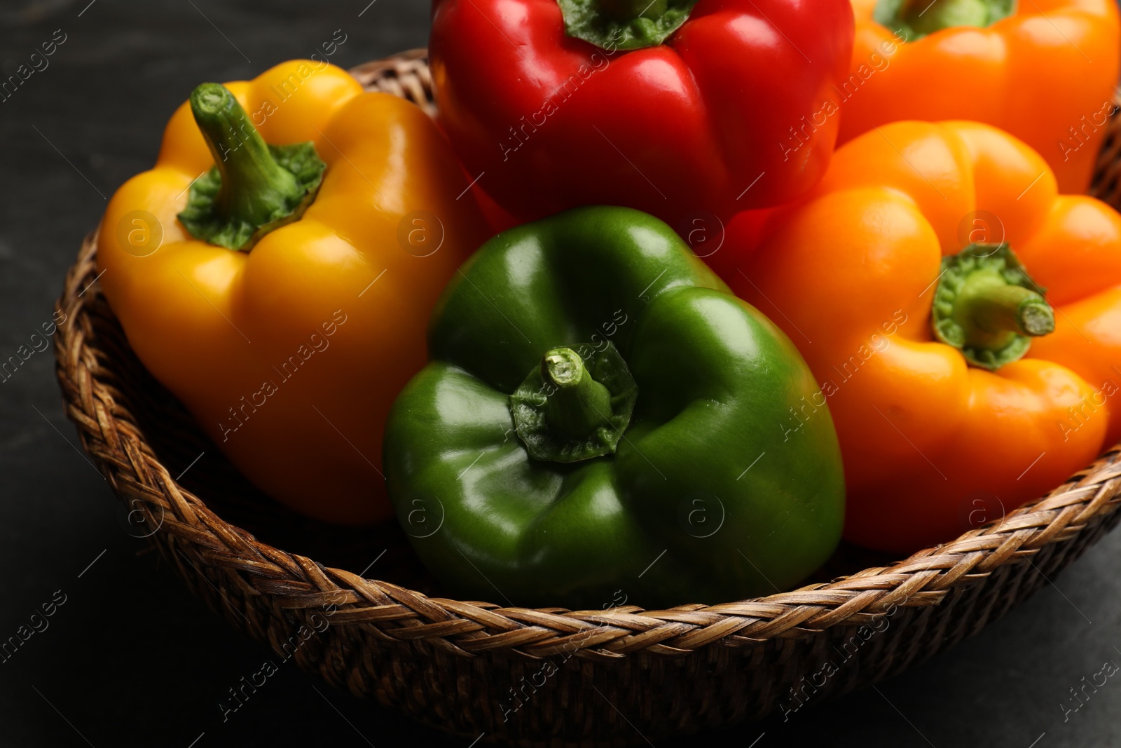 Fresh colorful bell peppers in wicker basket on dark table, closeup Photo of Fresh colorful bell peppers in wicker basket on dark table, closeup