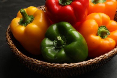 Photo of Fresh colorful bell peppers in wicker basket on dark table, closeup