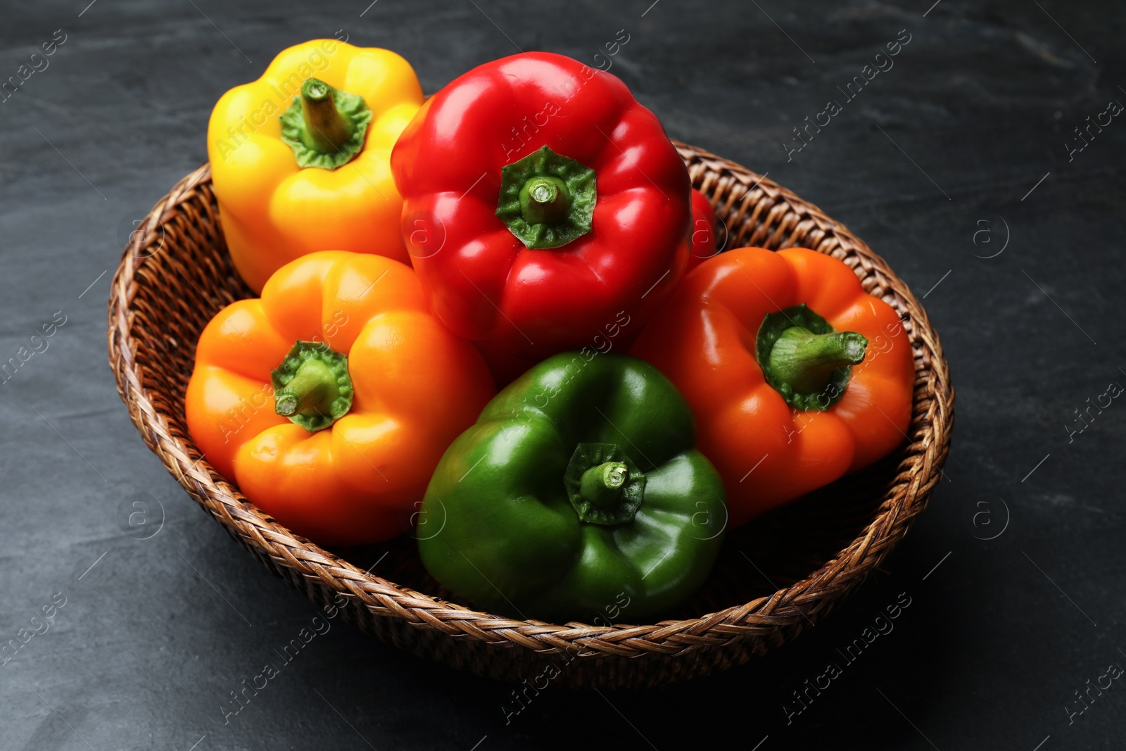 Fresh colorful bell peppers in wicker basket on black textured table, closeup Photo of Fresh colorful bell peppers in wicker basket on black textured table, closeup