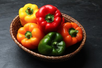 Photo of Fresh colorful bell peppers in wicker basket on black textured table, closeup