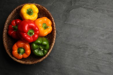 Photo of Fresh colorful bell peppers in wicker basket on black textured table, top view. Space for text