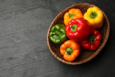 Photo of Fresh colorful bell peppers in wicker basket on black textured table, top view. Space for text