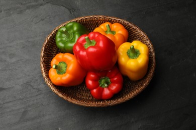 Photo of Fresh colorful bell peppers in wicker basket on black textured table, top view