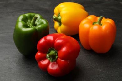 Photo of Fresh colorful bell peppers on black textured table, closeup
