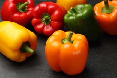 Photo of Fresh colorful bell peppers on black textured table, closeup