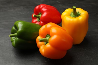Photo of Fresh colorful bell peppers on black textured table, closeup