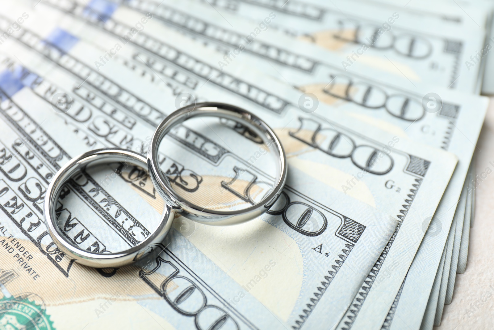 Two silver wedding rings and dollar banknotes on white table, closeup Photo of Two silver wedding rings and dollar banknotes on white table, closeup