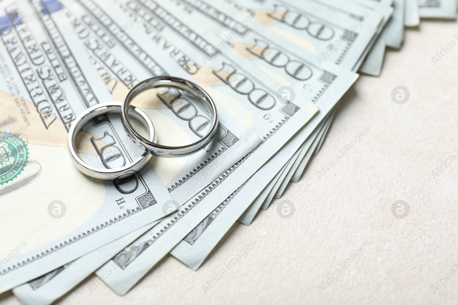 Two silver wedding rings and dollar banknotes on white table, closeup. Space for text Photo of Two silver wedding rings and dollar banknotes on white table, closeup. Space for text