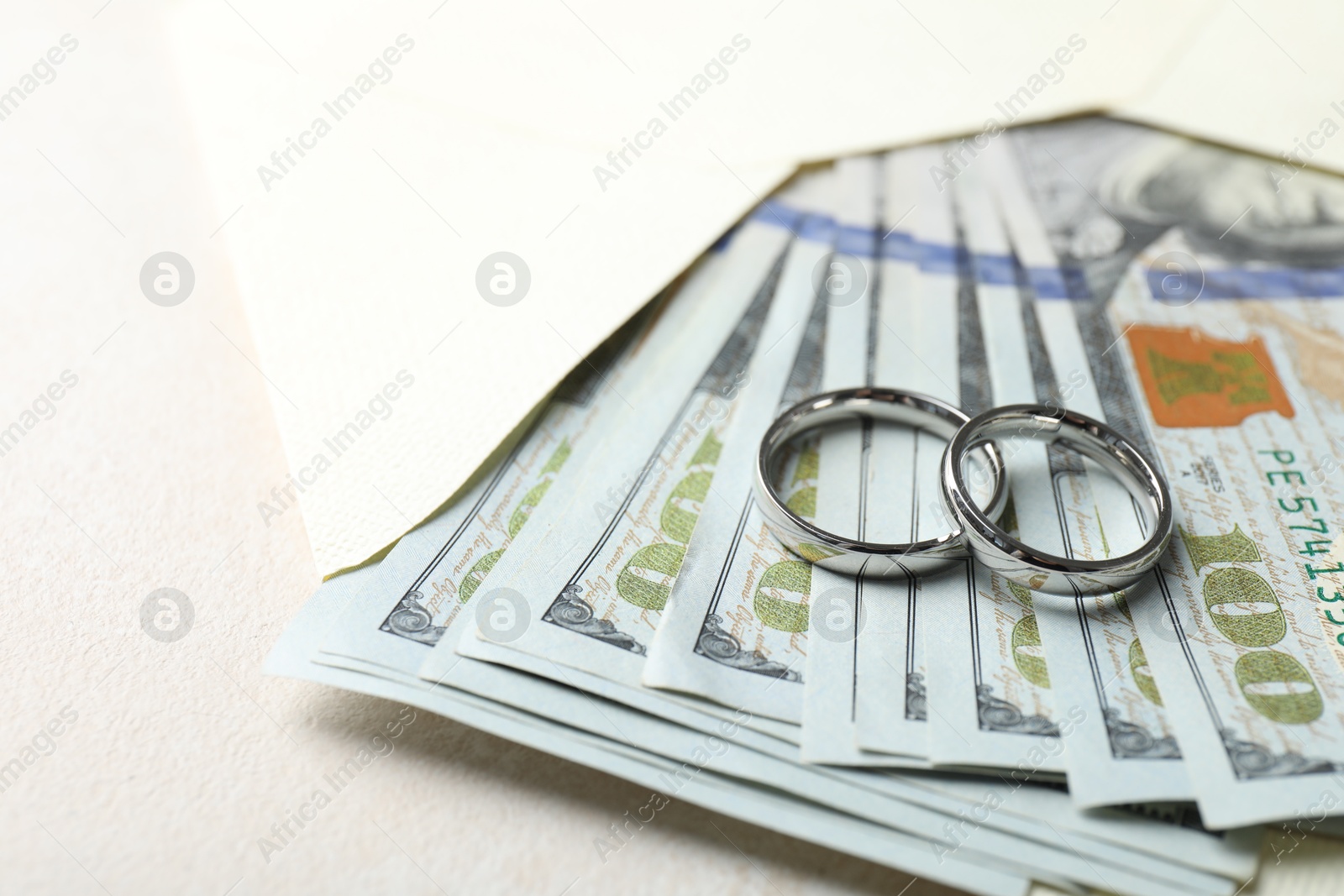 Photo of Two silver wedding rings, dollar banknotes and envelope on white table, closeup. Space for text