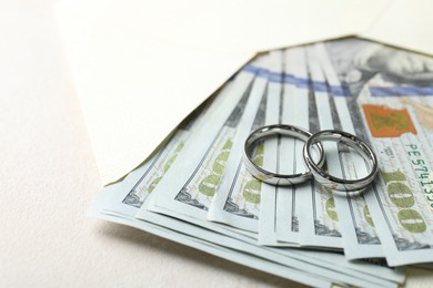 Photo of Two silver wedding rings, dollar banknotes and envelope on white table, closeup. Space for text