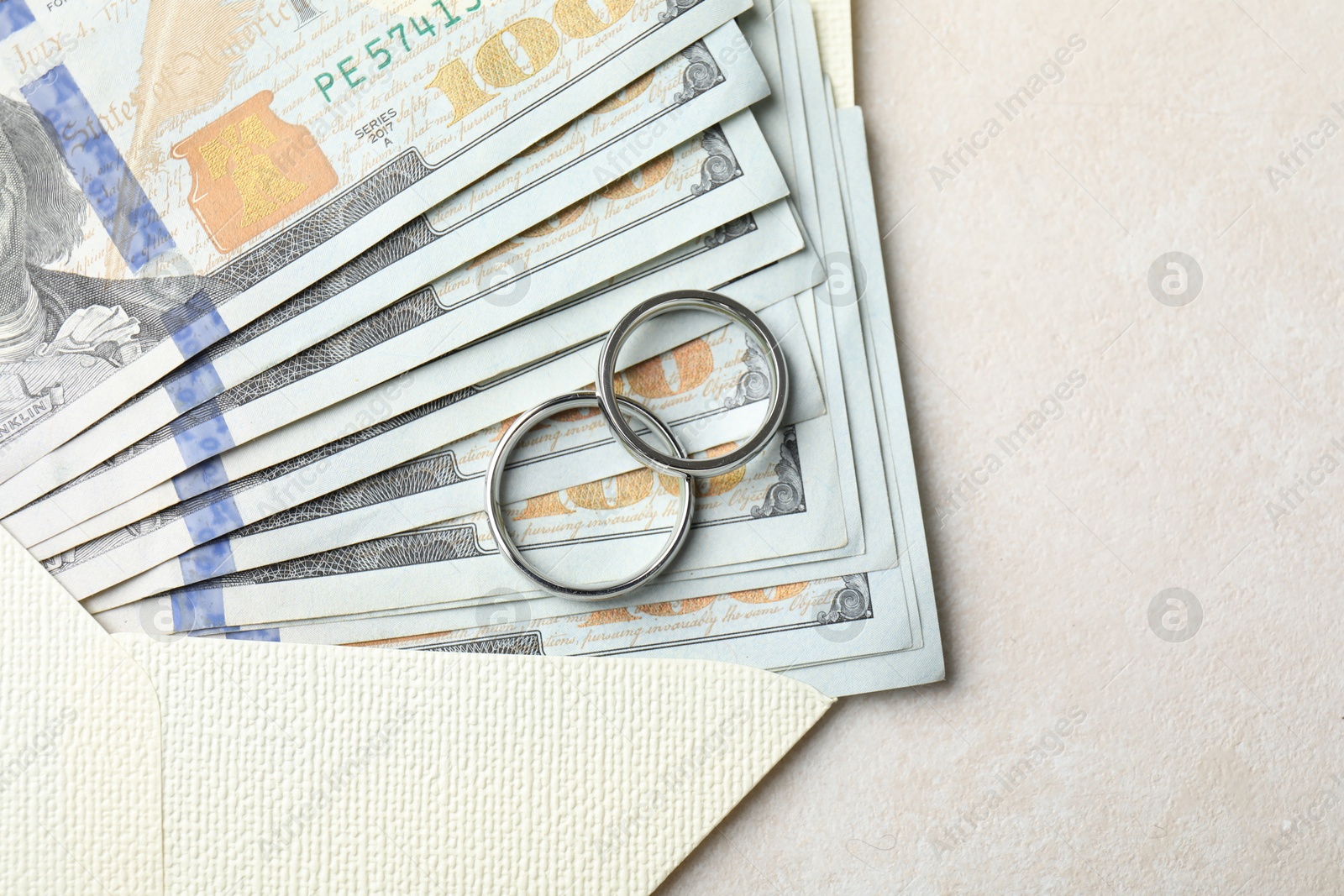 Photo of Two silver wedding rings, dollar banknotes and envelope on white table, top view. Space for text