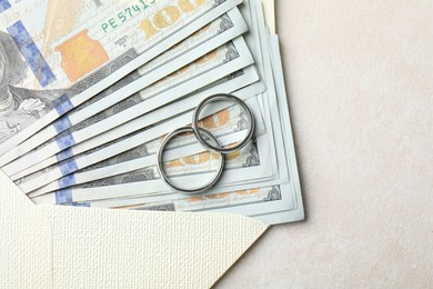 Photo of Two silver wedding rings, dollar banknotes and envelope on white table, top view. Space for text
