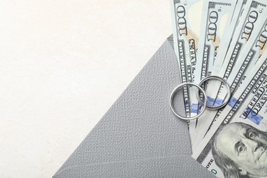 Photo of Two silver wedding rings, dollar banknotes and envelope on white table, top view. Space for text