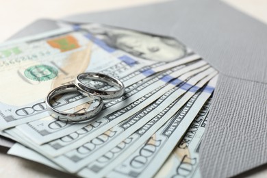 Photo of Two silver wedding rings, dollar banknotes and envelope on white table, closeup