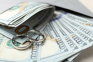 Photo of Two silver wedding rings, dollar banknotes and envelope on white table, closeup