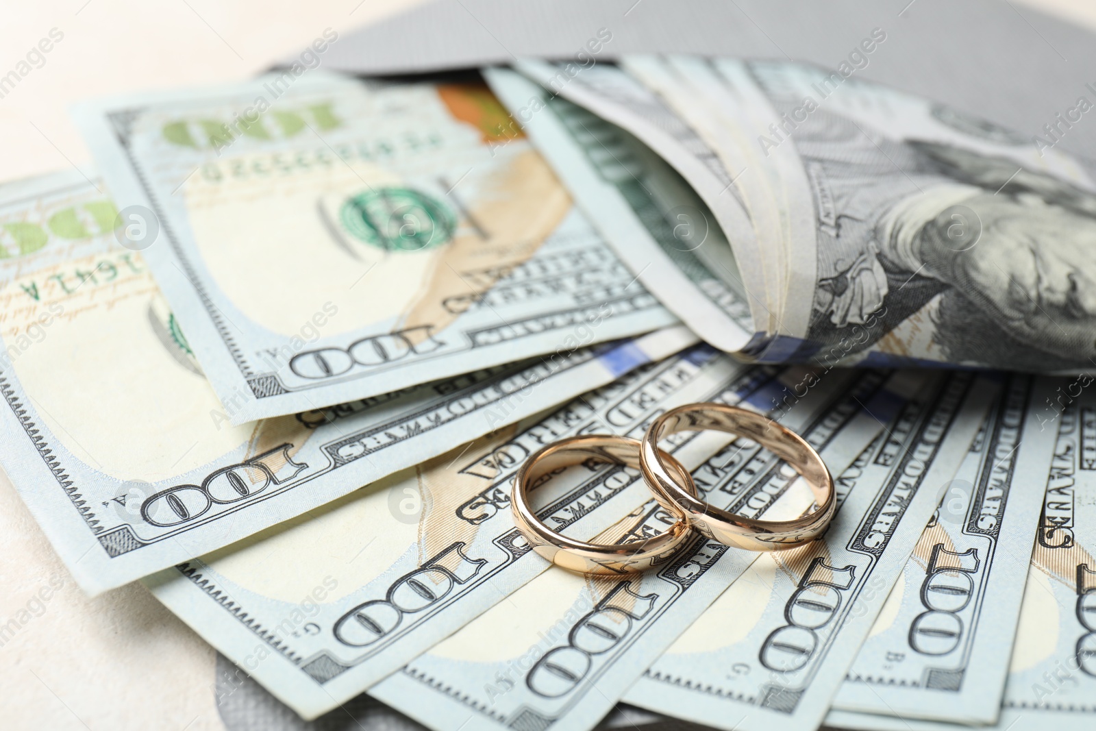 Photo of Two gold wedding rings, dollar banknotes and envelope on white table, closeup