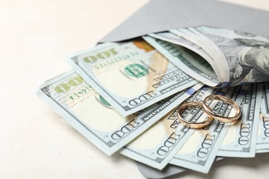Photo of Two gold wedding rings, dollar banknotes and envelope on white table, closeup