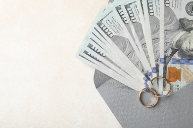 Photo of Two gold wedding rings, dollar banknotes and envelope on white table, top view. Space for text