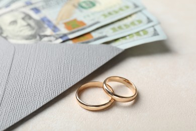 Photo of Two gold wedding rings, dollar banknotes and envelope on white table, closeup