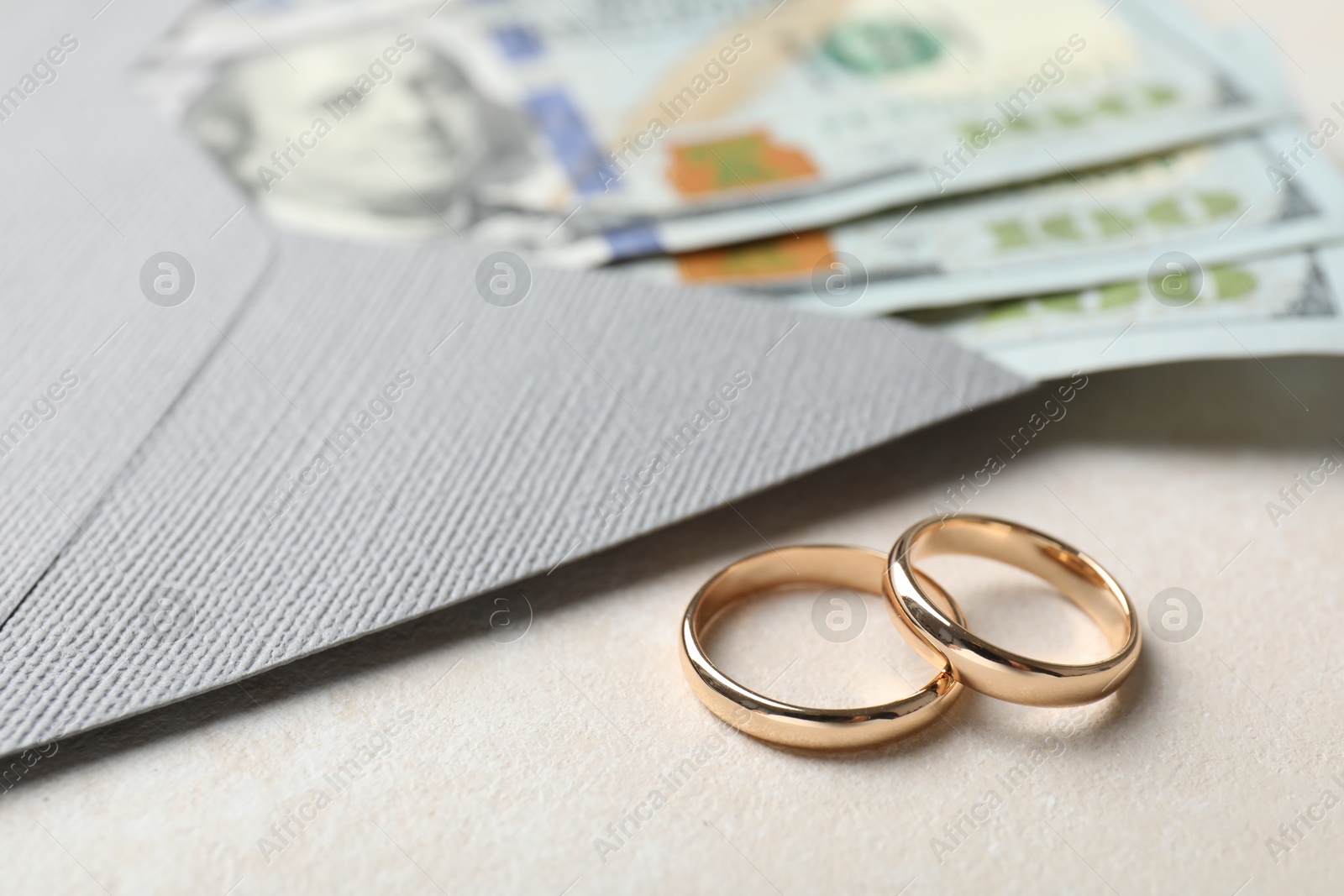 Two gold wedding rings, dollar banknotes and envelope on white table, closeup Photo of Two gold wedding rings, dollar banknotes and envelope on white table, closeup