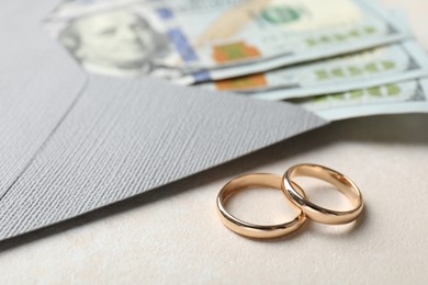 Photo of Two gold wedding rings, dollar banknotes and envelope on white table, closeup