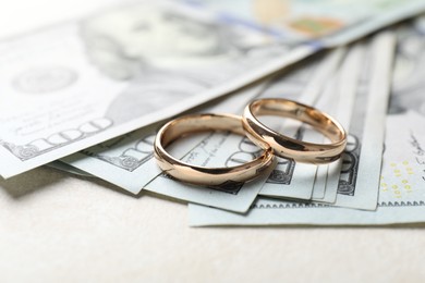 Two gold wedding rings and dollar banknotes on white table, closeup