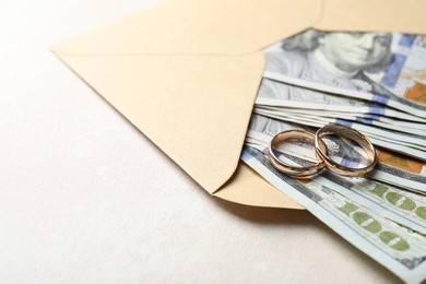 Photo of Two gold wedding rings, dollar banknotes and envelope on white table, closeup. Space for text