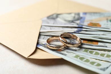 Photo of Two gold wedding rings, dollar banknotes and envelope on white table, closeup