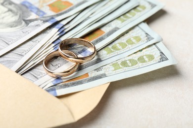 Photo of Two gold wedding rings, dollar banknotes and envelope on white table, closeup