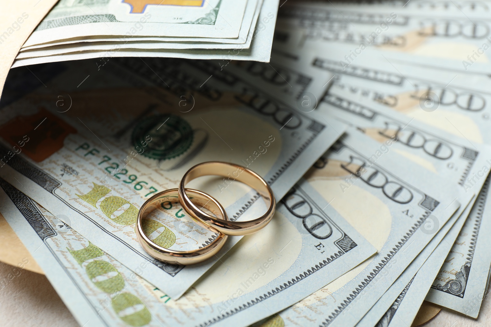 Photo of Two gold wedding rings, dollar banknotes and envelope on white table, closeup