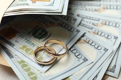 Photo of Two gold wedding rings, dollar banknotes and envelope on white table, closeup