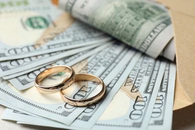 Photo of Two gold wedding rings, dollar banknotes and envelope on table, closeup