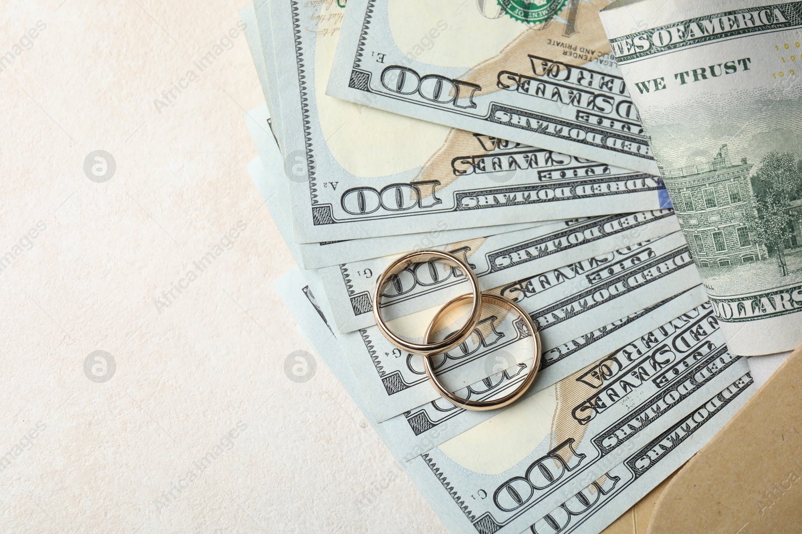 Photo of Two gold wedding rings, dollar banknotes and envelope on white table, top view. Space for text