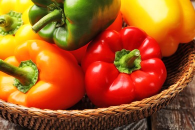 Photo of Fresh colorful bell peppers in wicker basket on table, closeup