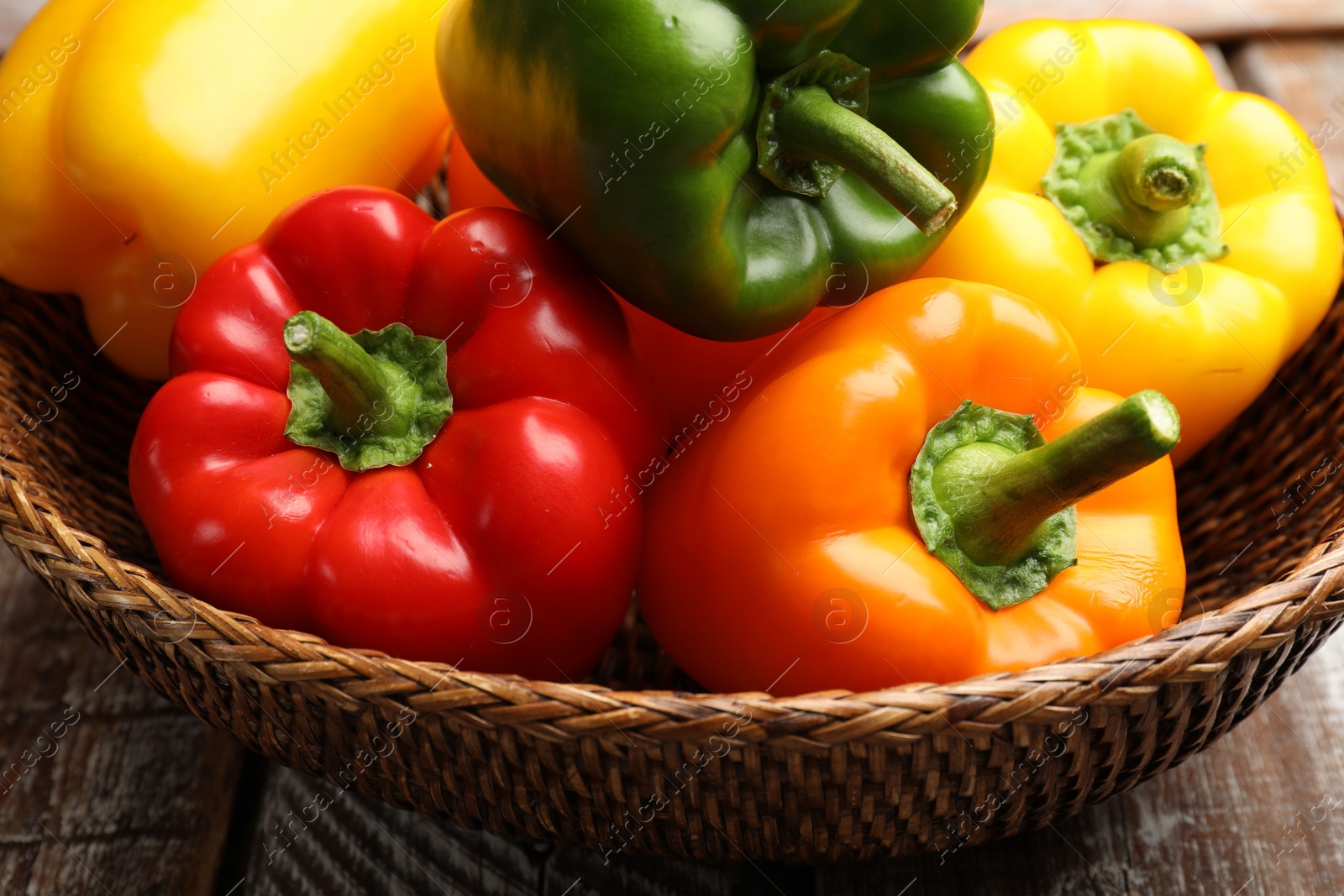 Photo of Fresh colorful bell peppers in wicker basket on table, closeup